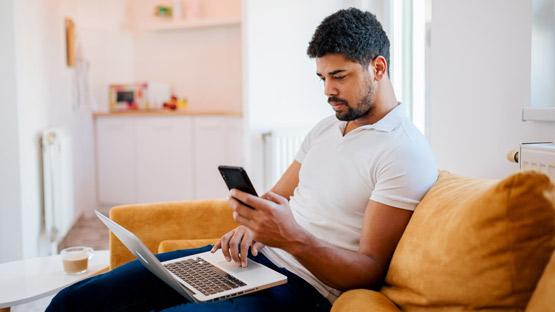 A man on a laptop looking at his phone